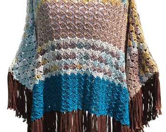 Puede incluir: Un poncho de ganchillo hecho a mano en una variedad de colores, incluyendo azul, marrón, amarillo y blanco. El poncho tiene un bajo con flecos y un diseño de tejido suelto y abierto. La prenda se exhibe en un maniquí blanco.