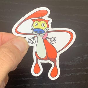 May include: A red and white cartoon character with a long, curled tail. The character has a blue nose, yellow eyes, and a pink tongue sticking out.