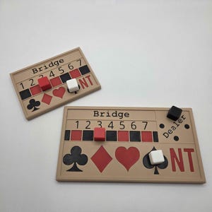 May include: Two beige Bridge game boards with red, black, and white game pieces. Each board has the word "Bridge" and numbers 1-7. Suit symbols are displayed below the numbers. One board has "NT" printed on it.
