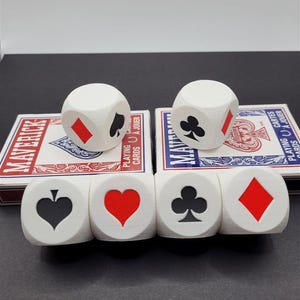 May include: Six white dice with black and red playing card symbols. The symbols are hearts, spades, clubs, and diamonds.