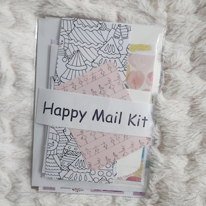 Puede incluir: Un kit Happy Mail en un paquete de plástico transparente. El kit incluye varios papeles estampados, pegatinas y páginas para colorear con diseños festivos y temáticos de ballet. El kit está envuelto con una banda blanca que dice "Happy Mail Kit".