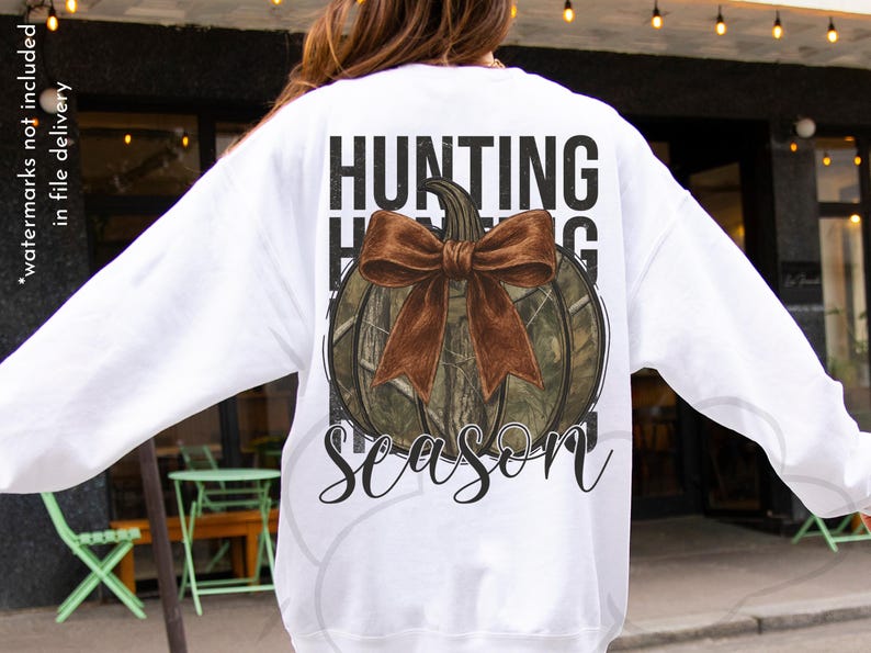 May include: White sweatshirt with a pumpkin graphic. The pumpkin has a camouflage pattern and a brown bow. The words "HUNTING SEASON" are printed above and below the pumpkin in a black font.