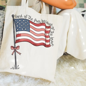 以下が含まれることがあります： 赤白青のアメリカ国旗と「land of the free, because of the brave」という文字が書かれた白いキャンバス地のトートバッグです。