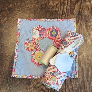 May include: A white ceramic mug with a black handle and the text "But First, Coffee" in a bold, black font. The mug is set against a blurred background, suggesting a cozy setting. The mug appears to be approximately 4 inches tall.