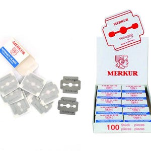 Könnte beinhalten: Eine Schachtel mit 100 Merkur Rasierklingen, mit einem roten und weißen Etikett, auf dem "Merkur Solingen" und "100 Stück - pieces - pièces - piezas" steht. Die Schachtel ist geöffnet und die Klingen sind sichtbar. Es befinden sich auch mehrere einzelne Klingen auf einer weißen Oberfläche.