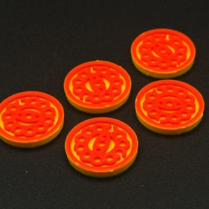 Op de afbeelding: Vijf gele en oranje ronde spelstukken met een rood ontwerp. Het ontwerp is een herhalend patroon van cirkels en ovalen.