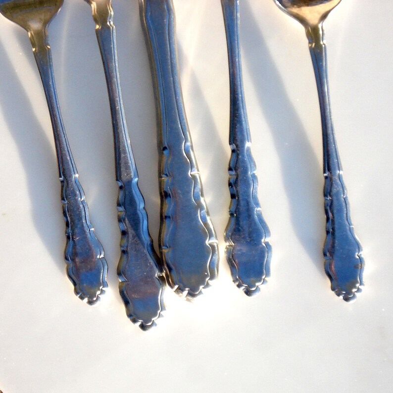 Puede incluir: Primer plano de cuatro piezas de cubiertos plateados con mangos ornamentados. Los mangos tienen un dise&ntilde;o decorativo festoneado.