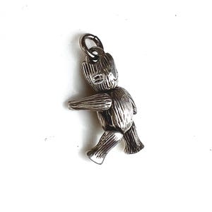 May include: A silver-colored charm in the shape of a walking figure with outstretched arms. The charm has a textured surface and a loop at the top for attaching to a necklace or bracelet. The figure is a stylized representation of a character.