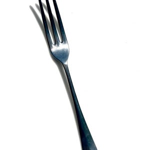 May include: A silver fork with three tines and a long, slender handle. The utensil is made of a shiny, metallic material and is designed for eating. The fork is angled slightly to the left against a white background.