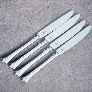 May include: Four silver dinner knives with a decorative handle and the text "GEORG JENSEN" on the blade.