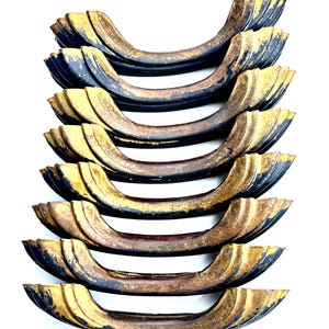 May include: A set of eight curved drawer pulls featuring a distressed finish with a dark black base color and worn gold-toned highlights on the edges. Each handle has a scalloped, tiered design with a central grip area and two mounting points.