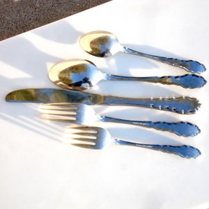 Puede incluir: Un juego de cinco cubiertos de plata plateada, que incluye un cuchillo, dos tenedores y dos cucharas. Los cubiertos tienen mangos adornados y decorativos.