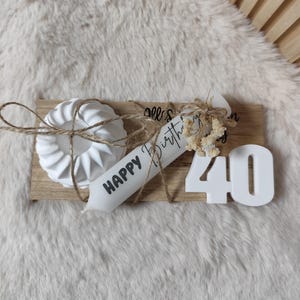 May include: White wooden board with a white candle that says "Happy Birthday" and a white number 40. There is a white cake mold on the board with twine wrapped around it.