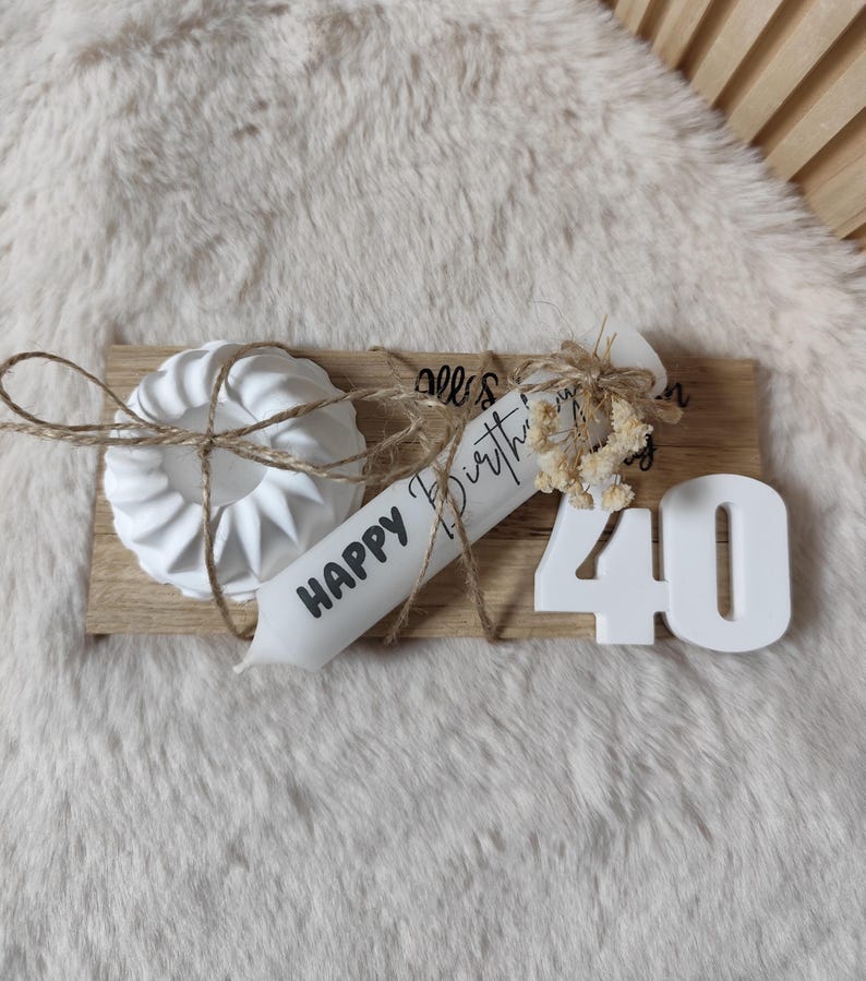 May include: White wooden board with a white candle that says "Happy Birthday" and a white number 40. There is a white cake mold on the board with twine wrapped around it.
