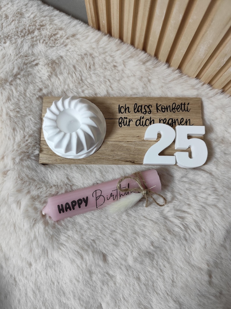 May include: A wooden tray with a white cake mold, white number 25 candles, and a pink candle that says "Happy Birthday". The tray has the text "Ich lass Konfetti f&uuml;r dich regnen" on it.