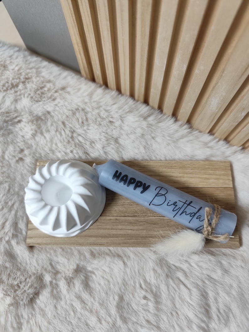 May include: A blue candle with the text "Happy Birthday" on it. The candle is sitting on a wooden tray with a white ceramic candle holder.