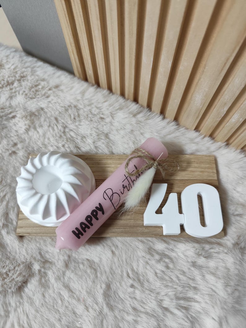 May include: A pink candle with the text "Happy Birthday" on it, a white ceramic candle holder, and white wooden number 40 on a wooden board.