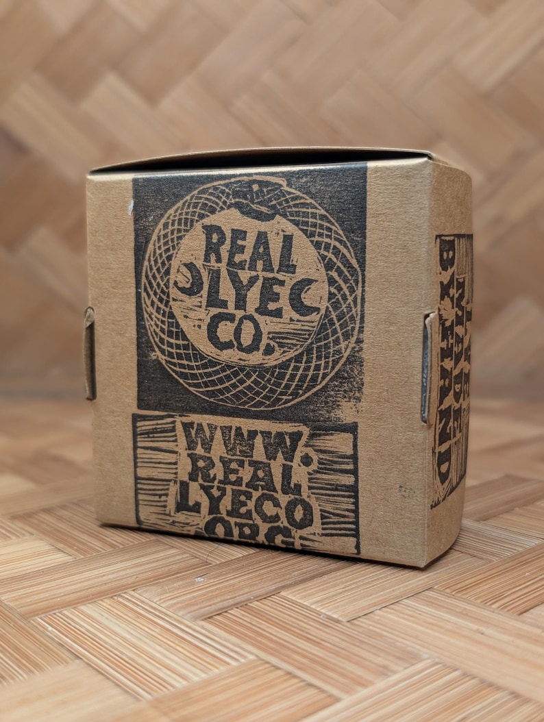 May include: A brown cardboard box with black printed text and graphics. The box features the words "REAL LYECO CO." and "WWW. REAL LYECO.ORG". The box is sitting on a bamboo surface.