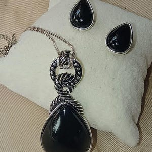 以下が含まれることがあります： シルバーカラーのジュエリーセット。涙型のペンダントネックレスと、お揃いのスタッドピアスが特徴です。ペンダントとピアスは、黒く光沢のある石がシルバーのフレームにセットされています。ネックレスチェーンは繊細です。