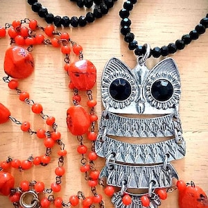 May include: A silver owl pendant necklace with black gem eyes and a black beaded chain. A separate necklace with orange beads and a third necklace with black beads are also visible.