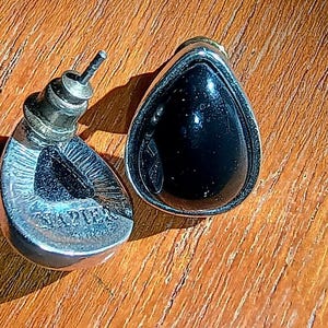 以下が含まれることがあります： 黒い石がシルバーカラーの金属フレームにセットされた、ヴィンテージのティアドロップ型イヤリングのペア。 イヤリングはポストバック式で、片方のイヤリングには「Napier」の文字が見えます。