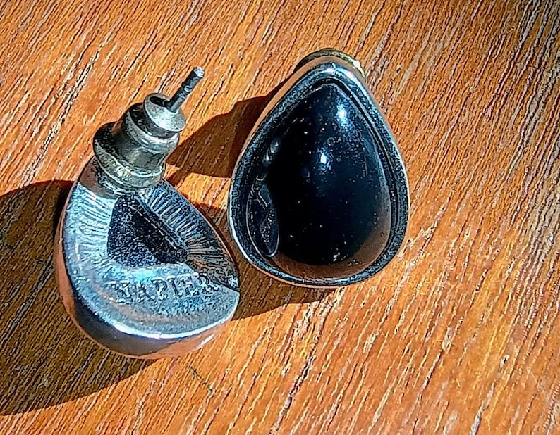 以下が含まれることがあります： 黒い石がシルバーカラーの金属フレームにセットされた、ヴィンテージのティアドロップ型イヤリングのペア。 イヤリングはポストバック式で、片方のイヤリングには「Napier」の文字が見えます。