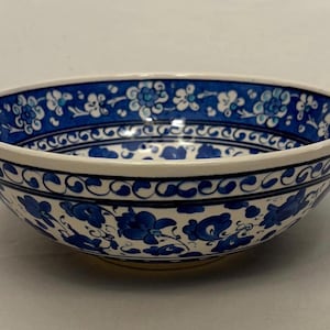May include: A ceramic bowl featuring a white base with intricate blue floral patterns and scrolling vine motifs. The interior rim displays a dense band of small flowers, while the exterior is decorated with larger blue blossoms and leaves.
