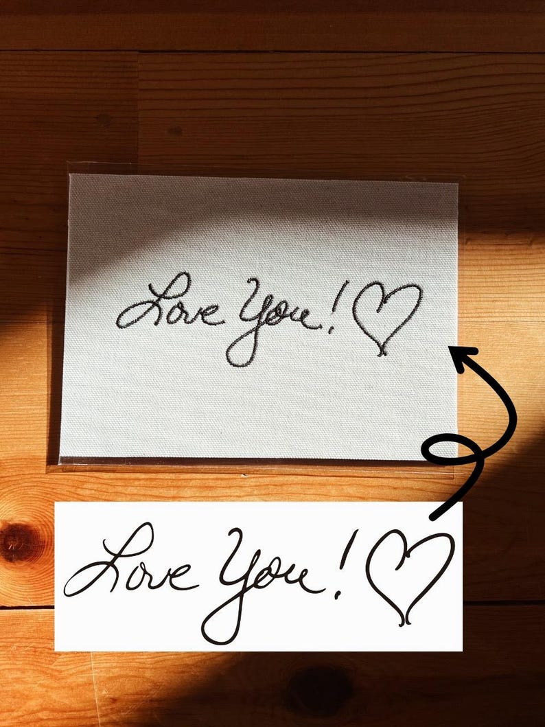 May include: A white card with the handwritten phrase "Love You!" and a heart symbol in black ink. The card is displayed on a wooden surface, with a second, similar card below.