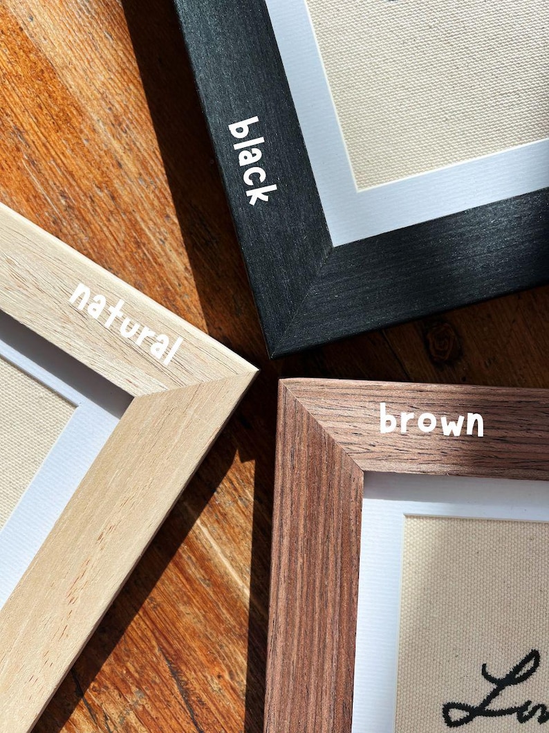 May include: Close-up of four framed art pieces with different frame colors: black, natural, and brown. The frames surround a canvas with white matting. The word "black", "natural", and "brown" are written on the frames.