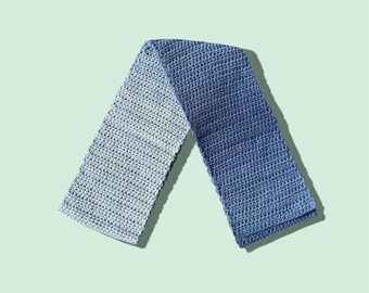 Puede incluir: Bufanda de ganchillo hecha a mano en tonos azules, que transita de claro a oscuro. La bufanda es rectangular, con un patrón de puntada texturizada. El artículo se muestra sobre un fondo verde claro.