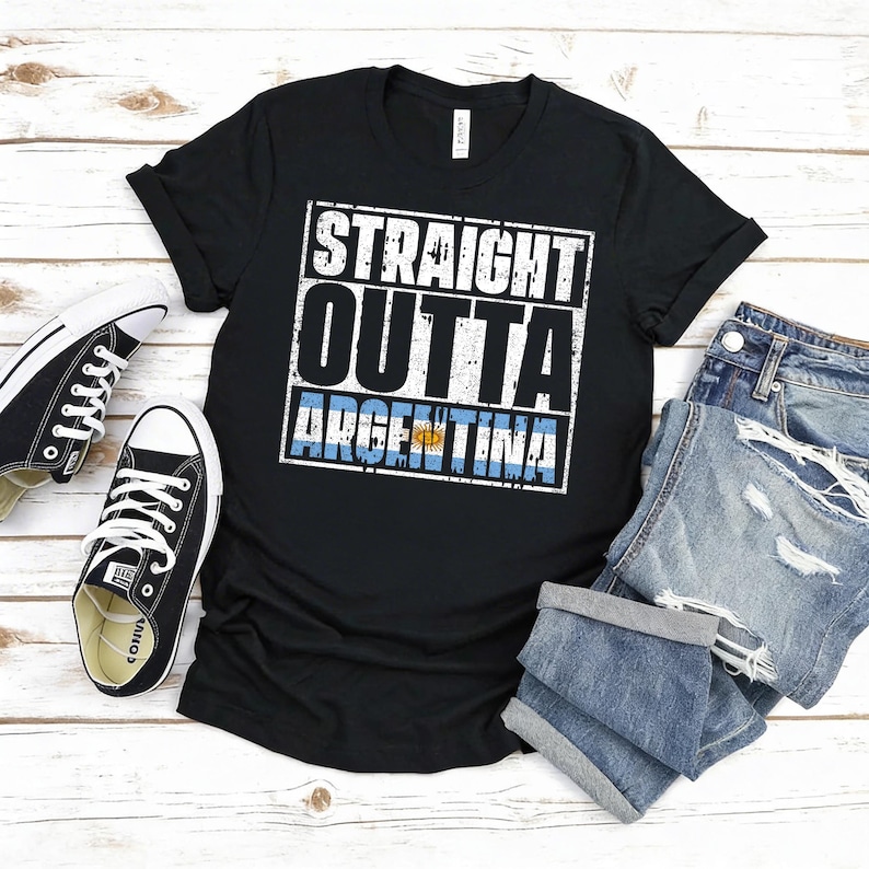 Puede incluir: Camiseta negra con el texto "STRAIGHT OUTTA ARGENTINA" en blanco, con un efecto desgastado. La bandera argentina se muestra debajo. La camiseta se combina con zapatillas negras y pantalones cortos vaqueros.