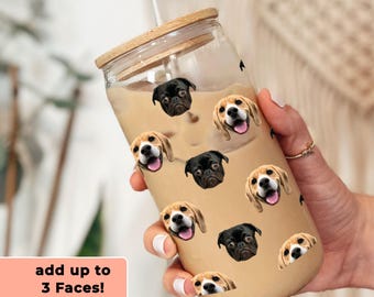 May include: A clear glass tumbler with a wooden lid and a straw. The tumbler is filled with a brown liquid and has a pattern of dog faces printed on it. The text "add up to 3 Faces!" is printed on a pink background.