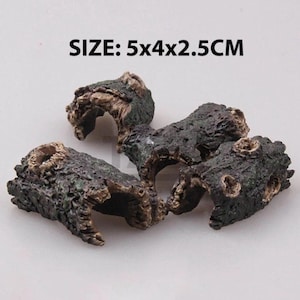 Può includere: Quattro pezzi di legno galleggiante artificiale, ciascuno con una superficie strutturata marrone scuro e verde. Il testo "SIZE: 5x4x2.5CM" è visibile nell'immagine. Questi pezzi decorativi sono adatti per acquari o terrari.