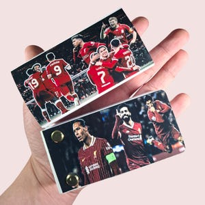 May include: Two rectangular magnets featuring images of a soccer team in red uniforms. One magnet shows players celebrating, while the other displays individual player portraits. Gold-colored button magnets secure the images.