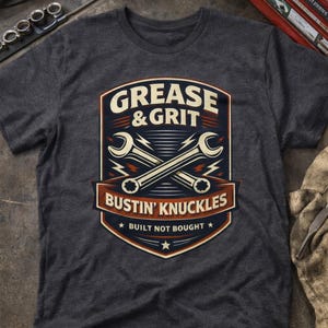 May include: Charcoal grey t-shirt with a graphic design. The design includes the words "Grease & Grit" and "Bustin' Knuckles" above crossed spanners. The phrase "Built Not Bought" is below the spanners. The design is in blue, red, and white.