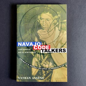 May include: A book titled "Navajo Code Talkers" with a portrait of a person in the background. The cover features text in blue, red, and white, with the subtitle "America's Secret Weapon in World War II." The author's name is Nathan Aaseng.
