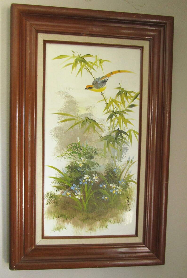 Wall Art
Vintage framed oil painting on canvas with solid wood frame depicting a bird  in a grove of bamboo above pretty blue and white flowers. It is a vintage hand painted decorative item, signed on the lower right corner.