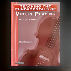 May include: A book titled "Teaching the Fundamentals of Violin Playing" by Jack M. Pernecky. The cover features a violin illustration in shades of brown and red. The contributing editor is Lorraine Fink.