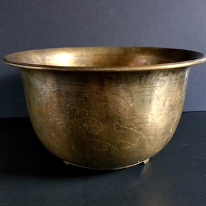 May include: A brass planter with an etched floral design. The planter has a rounded bottom and a wide rim.