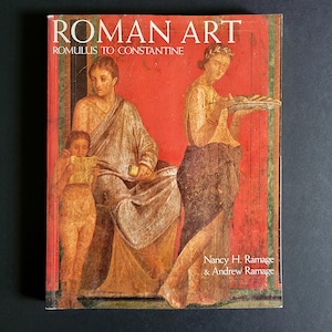 May include: A hardcover book titled "ROMAN ART" with the subtitle "ROMULUS TO CONSTANTINE." The cover features a red background with classical artwork depicting figures in draped clothing. The authors' names, Nancy H. Ramage & Andrew Ramage, are printed at the bottom.