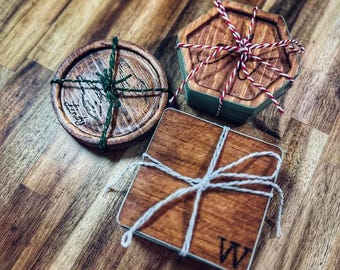 Può includere: Tre sottobicchieri in legno con diversi design. Un sottobicchiere è rotondo e ha uno spago verde e bianco legato intorno. Un altro sottobicchiere è esagonale e ha uno spago rosso e bianco legato intorno. Il terzo sottobicchiere è quadrato e ha uno spago bianco legato intorno. Il sottobicchiere quadrato ha la lettera "W" incisa.