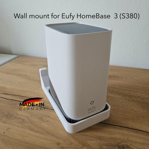 Könnte beinhalten: Weiße Wandhalterung für Eufy HomeBase 3 (S380). Die Halterung besteht aus weißem Kunststoff und hat eine rechteckige Basis und eine vertikale Stütze. Der Text "Wall mount for Eufy HomeBase 3 (S380)" ist sichtbar.