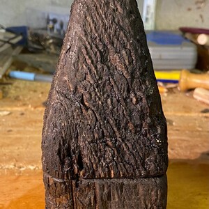 May include: A dark brown wooden object with a pointed top and a square base. The object is made of rough-hewn wood and has a rustic appearance.