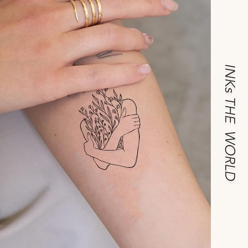 May include: A temporary tattoo of a line drawing of a person hugging themself with flowers growing from their body. The tattoo is on a person's arm. The text "INKS THE WORLD" is visible in the background.