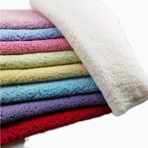 May include: A stack of colorful fuzzy fabric swatches in shades of pink, blue, yellow, green, purple, and red. The fabric is soft and plush, perfect for crafting or sewing projects.