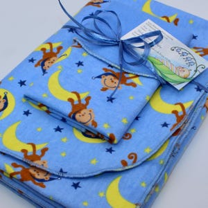 May include: A set of three blue fleece baby blankets with a yellow crescent moon and brown monkey pattern. The blankets are folded and tied with a blue ribbon. The tag reads "Sleepy Makers & Pure Chaos".