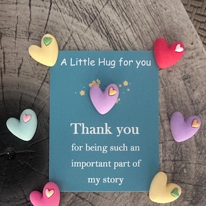 May include: A teal card with the text "A Little Hug for you" and "Thank you for being such an important part of my story." The card is surrounded by heart-shaped decorations in various colors, including yellow, pink, and purple.