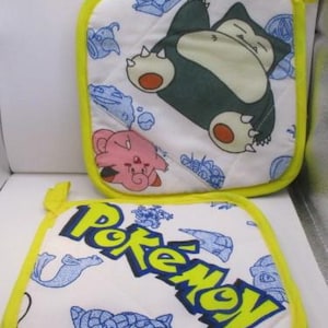 May include: Two white cotton pot holders with yellow trim. One pot holder features a blue and yellow Pokemon logo and a blue and white illustration of a Pokemon character. The other pot holder features a pink and white Pokemon character and a green and white Pokemon character.