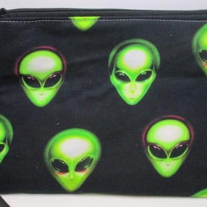 May include: Black zippered pouch with a repeating pattern of green alien faces. The pouch has a black strap.