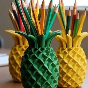 May include: Three pineapple-shaped pencil holders, one green and two yellow, filled with colorful pencils. The pencils are various colors, including green, yellow, orange, and red. The holders are made of a textured material.
